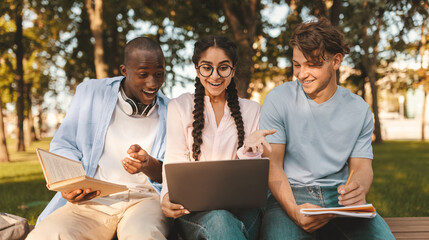 Accepted students. Joyful diverse friends celebrating success with laptop computer outdoors, cheering successful exam pass, sitting in parkland