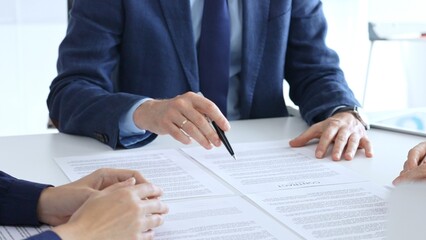 Businessman or lawyer pointing into contract papers with black pan and discussing documents with colleagues in a bright office. Business people concept