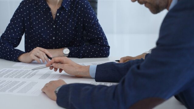 Corporate professionals analyzing contract details, gesturing toward key points while negotiating partnership terms in modern office boardroom - Powered by Adobe
