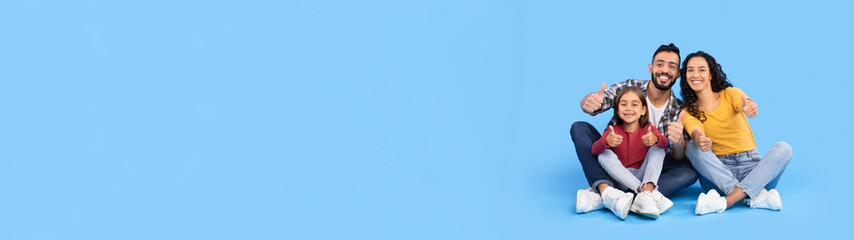 We Like It. Happy Middle Eastern Family Gesturing Thumbs Up Posing And Approving Something Together Smiling To Camera Sitting Over Blue Background. Great Offer Concept. Studio Shot