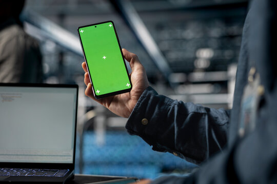 Close up of server farm software developer using mockup phone, waiting for code to finish compile. Data center employee checking mobile apps on green screen smartphone to relax