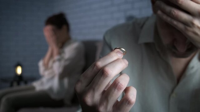 Frustration couple with divorced ring. A sad husband holds a wedding ring in his hands, his wife sits behind him, offended