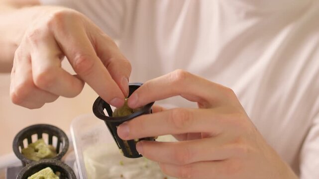 Close-up of male hands transplanting young green sprout into rockwool cube inside a net pot, ready for insertion into hydroponic system for indoor sustainable gardening. Shooting in slow motion.