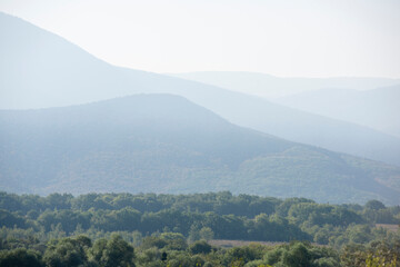 Obraz premium Silhouettes of mountains in the dawn haze and trees in the foreground