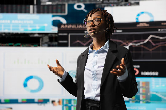 Business coach hosting key note presentation with live audience, pitching investing strategy at convention. African american businesswoman showing forecasting graphs at business event