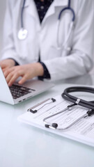 Stethoscope is lying on the glass table while doctor woman is working with laptop computer on the...
