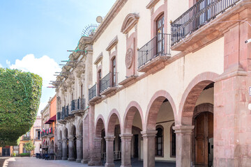 A street with a row of buildings, one of which has a balcony. The buildings are old. Historic center of Queretaro, colonial architecture, decorations for the celebration of Mexico's Independence Day.