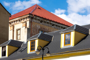 contrast of renovated modern roof with dormer windows and old weathered historic building behind