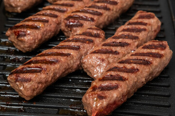 Grilled Chevapchichi (Cevapi) on a Black Cast Iron Griddle, Close-up of Sizzling Meat Kebabs with Grill Marks, Balkan Cuisine BBQ Food, Overhead Macro Stock Image
