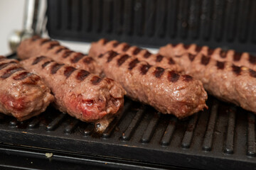 Close-up of traditional grilled minced meat rolls (Mici or Cevapcici) cooking on a hot grill pan, showing rich grill marks and sizzling texture, perfect for food, cooking, Eastern European cuisine, an