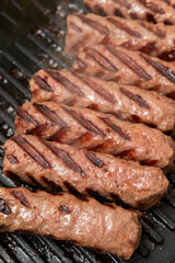 Grilled meat sausages, traditional Balkan ćevapi cooking on barbecue grill, close-up of juicy grilled meat with grill marks, concept of homemade cuisine, street food, and outdoor cooking photography