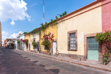 Naklejka premium A street with a row of yellow buildings and a green door. The street is empty and the sky is blue. Historic center of Queretaro, colonial architecture, decorations for the celebration of Mexico's Inde