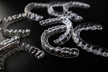 Multiple transparent dental aligners (invisible braces) scattered in a dramatic low-key studio setting on a deep black background, showcasing modern orthodontic technology for dentistry, healthcare, a