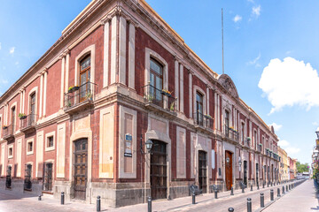 Fototapeta premium A large building with a red and white facade. The building has a lot of windows and balconies. Historic center of Queretaro, colonial architecture, decorations for the celebration of Mexico's Independ