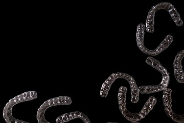 Multiple transparent dental aligners (invisible braces) scattered in a dramatic low-key studio setting on a deep black background, showcasing modern orthodontic technology for dentistry, healthcare, a