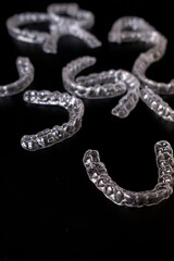Clear invisible dental aligners for orthodontic correction and teeth straightening, scattered on a black background, perfect for dentistry advertising, medical stock photos, and healthcare concepts