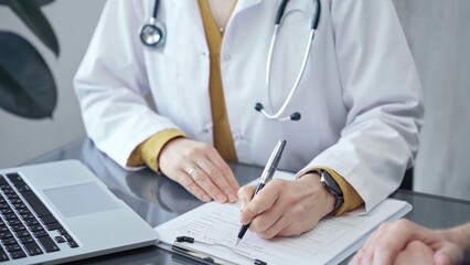 Fototapeta premium Doctor completing paperwork with patient. Close-up of a doctor's hands with forms, imparting information to a laptop. Medicine and health care concept