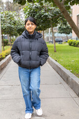 A teenager in a black jacket and blue jeans stands in front of a gate