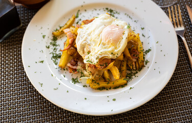 Appetizing scrambled eggs with bacon and french fries served on plate