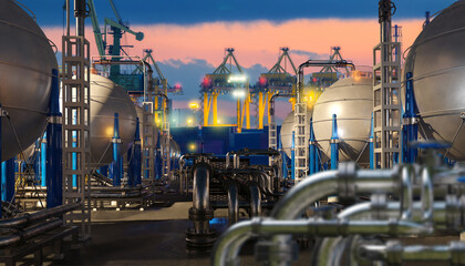Liquefied natural gas terminal with spherical storage tanks, pipelines and cranes at port during sunset operations. LNG storage, transport, energy industry.