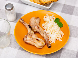 Portion of hearty lunch on plate - pieces of roasted rabbit legs competed with rice porridge