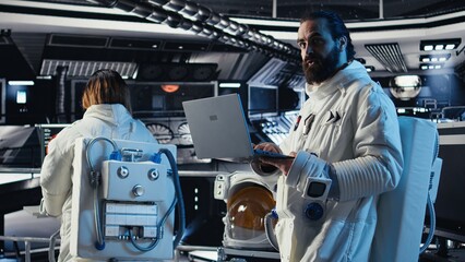 Astronaut reviewing onboard analytics on laptop before stepping out for scheduled operations outside space station. Cosmonaut verifying mission parameters after landing on alien planet © DC Studio