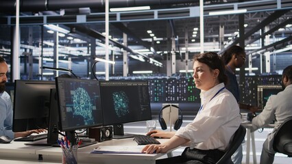 Data center software developer using PC to monitor neural network AI visualization. Woman working in server room using computer to oversee rigs powering machine learning processes, camera A