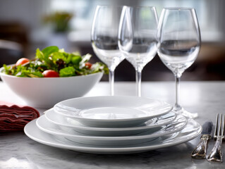 Elegant dining table setting with stacked white plates, empty wine glasses, fresh mixed green salad, and silverware arranged on marble surface in bright room