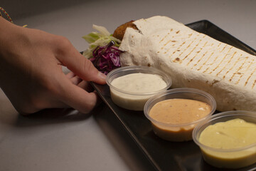 A hand reaches out to a plate of delicious food that has three enticing dipping sauces positioned beside it