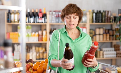 Adult woman buyer chooses tomato and pomegranate juices in bottle in grocery store