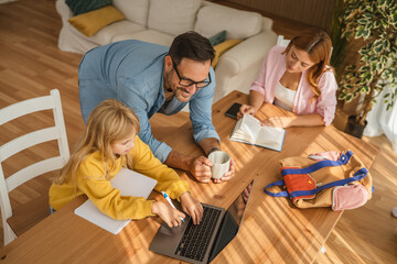 Family helping daughter studying homework with laptop at home