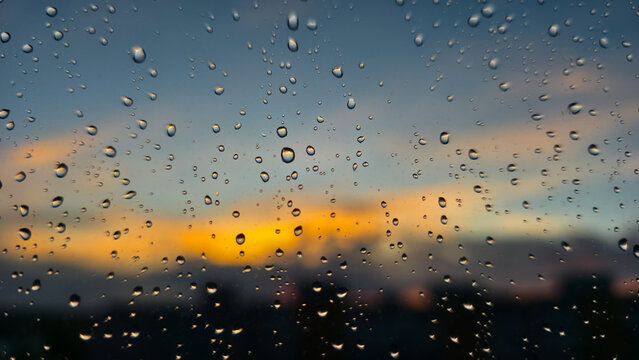 Close-up raindrops on window against glowing sunset sky. Warm light contrasts with cool tones, creating a tranquil and reflective mood of evening calm after gentle rain.