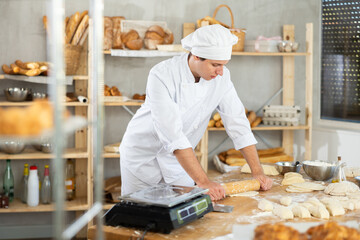 Making yeast dough in bakery - young male baker rolling out dough with a rolling pin