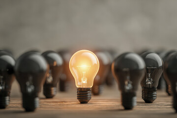 A glowing incandescent bulb shining brightly among multiple unlit bulbs symbolizing innovation, leadership, and standing out in a sea of sameness on wooden surface
