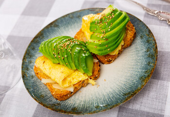 Toast with fresh avocado cheese and scrambled eggs served on platter