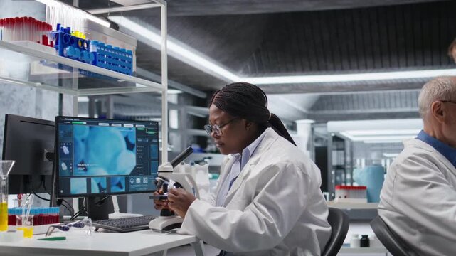 African american chemist analyzing molecular samples in a lab, using professional microscope. Healthcare innovation and biochemistry experiments represent scientific method and discovery. Camera A.