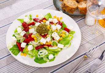 Appetizing salad of fresh vegetables served with feta cheese and pesto on plate