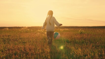 Girl run in meadow kicking ball with her foot. Cheerful child running in nature, playing football with ball. Sports lifestyle for child in nature. Active girl child. Family in park. Children football
