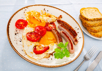 Homemade hearty breakfast - fried eggs with frankfurter and tomato. Dish is decorated by spring of cilantro parsley