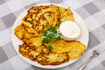 Delicious zucchini pancakes with bowl of sour cream served on plate