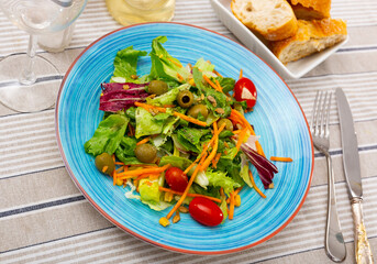 Vegetable side dish, salad of chopped cabbage leafy vegetables, grated carrots, whole olives and cherry tomatoes. Summer snack seasoned with olive oil