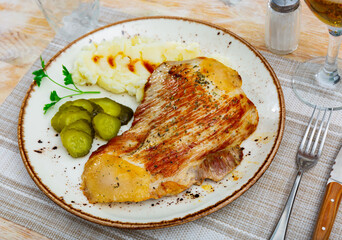 Appetizing piece of fried pork with marinated cucumber and potatoes served on plate