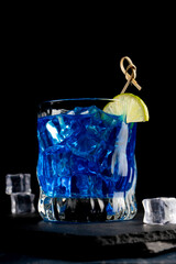 Colorful blue cocktail in a glass with a slice of lime on a black background
