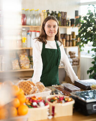 Teenage girl seller in apron standing at counter in grocery store..