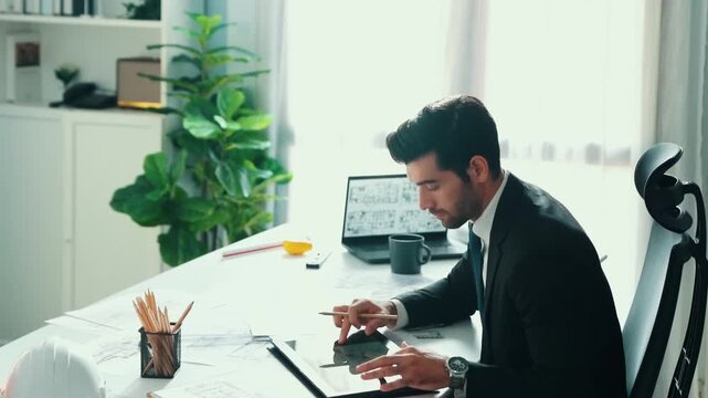 Architect engineer using laptop planning house design at office while sitting at meeting table with blueprint and equipment scatter around.Skilled civil engineer working at blueprint. Alimentation.