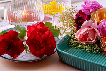 Colorful roses in a turquoise ceramic baking dish and on a plate with champagne glass. Floral composition for special occasion.