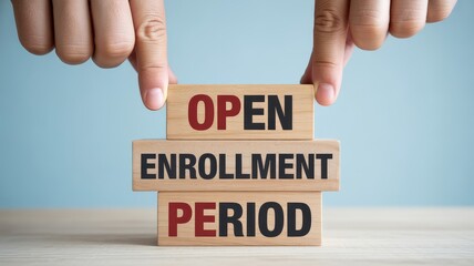 Hands placing wooden blocks spelling OPEN ENROLLMENT PERIOD for insurance or educational registration