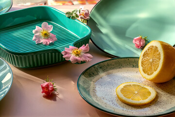 Turquoise ceramic baking dish with pink wild rose flowers and fresh lemon slices. Cooking and kitchenware concept. Home cooking tool.