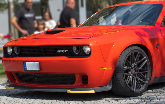 Polska, Ostrowiec Świętokrzyski, 20 lipca 2025, 14:22. DODGE CHALLENGER HELLCAT &ndash; Amerykański czerwony samoch&oacute;d pony car porusza się po brukowanej ulicy.W&oacute;z charakteryzuje się agresywnym przodem 
