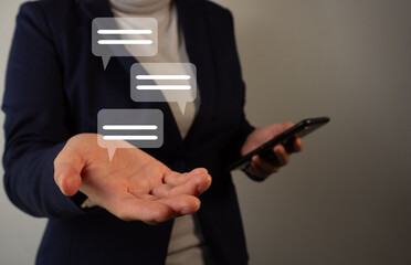 Businesswoman holding a cell phone while holding chat icons with the other hand